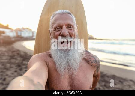 Glücklicher Senior-Surfer, der Selfie macht und Spaß beim Surfen bei Sonnenuntergang hat - Senioren Gesundheit Menschen Lebensstil und Extremsportkonzept Stockfoto