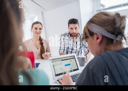 Zuverlässige junge Mitarbeiter denken an Lösungen und neue erfolgreiche Ideen und teilen sich gleichzeitig den Schreibtisch eines modernen Büroraumes für digitale Nomaden Stockfoto