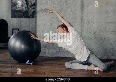 Sportliche rothaarige Mädchen tun Stretching-Übungen mit Fitness-Ball Stockfoto