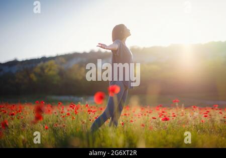 Junge schöne Frau mit erhobenen Armen im Frühjahr Mohnfeld. Sanfte Farben. Nachdenkliche, entspannte Atmosphäre. Stockfoto