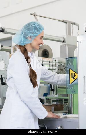 Nahaufnahme der Hand einer Fertigungsingenieurin, die die Einstellungen einer Industriemaschine während der Arbeit in einer modernen Kosmetikfabrik anpasst Stockfoto