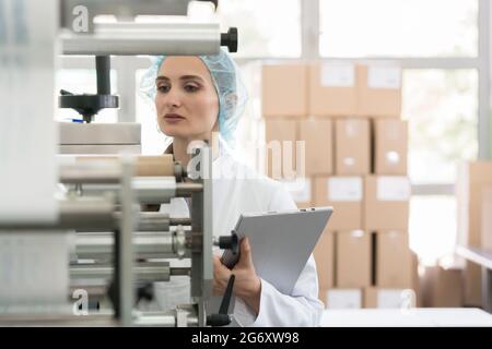 Weibliche Herstellung Supervisors besorgt, bei der Überprüfung der Anlagen und die Produktion bei der qualitaetskontrolle im Inneren einer Kosmetik Factory Stockfoto