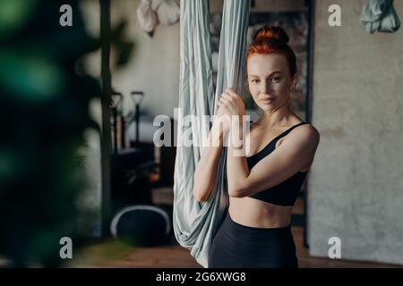 Junge Frau, die im Studio für Antigravitationsyogaübungen bereit ist und in die Kamera schaut Stockfoto