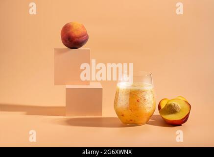 Fruchtsaft aus einem frisch reifen Pfirsich in einem Glas auf einem trendigen Podium orangen Hintergrund. Gesunder Lebensstil Stockfoto