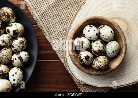 Wachteleier in Holzschüssel und auf dunklem Teller auf Holz; kleine gefleckte Eier; Delikatesse; natürliches rustikales Konzept Stockfoto