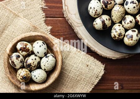 Wachteleier in Holzschüssel und auf dunklem Teller auf Holz; kleine gefleckte Eier; Delikatesse; natürliches rustikales Konzept Stockfoto