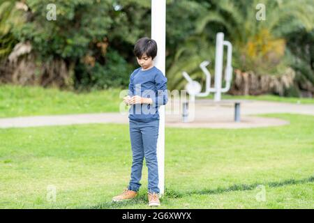 Trauriges Kind, das alleine steht und in den Park hinunterschaut. Einsamer kleiner Junge, der Grashalme in den Händen hält. Stockfoto