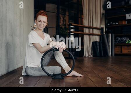 Lächelnde junge sportliche Frau mit Pilates-Ring genießt das Training im Fitnessstudio Stockfoto