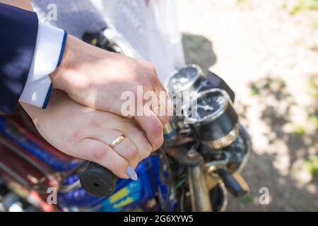 Hände eines verheirateten Paares mit Ringen, die auf dem Motorrad wegreiten. Stockfoto