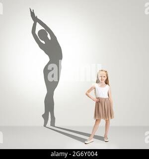 Kindheit und Traum von der großen und berühmten Zukunft. Konzeptuelles Bild mit Mädchen und Schatten der fittigen weiblichen Balletttänzerin auf hellgrauem Hintergrund Stockfoto