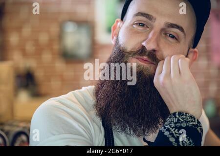 Nahaufnahme Porträt einer jungen und modischen männlichen Hairstylist mit Cool hipster Bart und Schnurrbart lächelnd während Kamera schaut mit Vertrauen Stockfoto