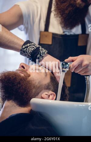 Close-up in die Hände eines erfahrenen mann Friseur, Haare waschen zu einem glücklichen Kunden vor oder nach dem Haarschnitt in einem modernen Beauty Salon Stockfoto