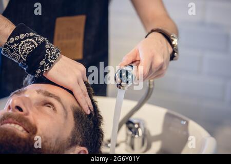 Close-up in die Hände eines erfahrenen mann Friseur, Haare waschen zu einem glücklichen Kunden vor oder nach dem Haarschnitt in einem modernen Beauty Salon Stockfoto