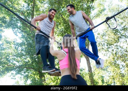 In der Rückansicht zeigt eine fittige Frau, die ihren beiden männlichen Freunden beim extremen Training im Freien in einem modernen Calisthenics-Park den Daumen hoch zeigt Stockfoto