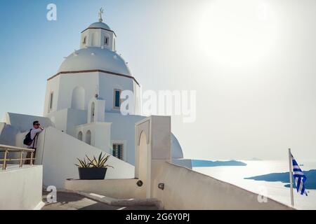 Mann Tourist genießen traditionelle Architektur zu Fuß an der weißen Kirche auf Santorini Insel mit Meereslandschaft in Fira. Griechische Flagge Stockfoto