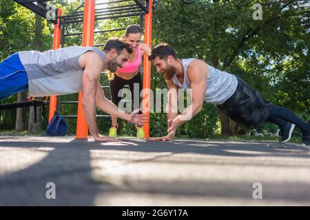 Zwei passen junge Männer klatschen Hände vom Gesicht Ganzkörperstütz während Partner Training durch ihren Freund draußen im Park motiviert zu Gesicht Stockfoto