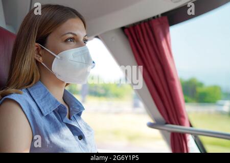 Fahren Sie sicher mit öffentlichen Verkehrsmitteln. Junge Frau mit KN95 FFP2 schützender Gesichtsmaske, die während ihrer Reise durch das Busfenster schaut. Stockfoto