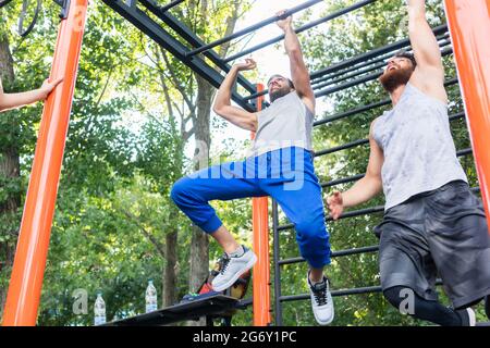 Low-Winkel auf zwei starke und wettbewerbsfähige Männer Ausübung auf Monkey Bars für den Oberkörper in einem modernen Calisthenics Park Stockfoto