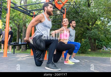 Volle Seitenansicht von drei entschlossenen Freunden, die Stretching-Übungen für Beine machen, als Aufwärmen oder Abkühlen Routine im Freien in einer modernen Fitness Stockfoto
