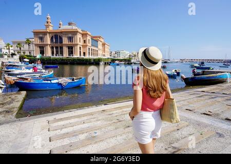 Junge Frau, die das Margherita Theater und die Fischerboote im alten Hafen von Bari, Region Apulien, Italien, anschaut Stockfoto