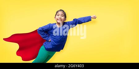 Konzept der starken Helden. Das asiatische Mädchen Modell in Aktion mit Superheros Kleid und trägt Gesichtsmaske auf gelb isolierten Hintergrund (einschließlich Pfad) Stockfoto