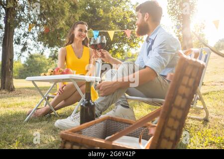 Junge und schöne Paar in Liebe Toasten mit Rotwein, während Sie sitzen auf Klappstühlen beim romantischen Picknick im Grünen Stockfoto