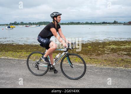 Seitenansicht einer jungen Frau, die in West Sussex, England, mit einem Helm auf dem Fahrrad oder Fahrrad unterwegs ist. Stockfoto