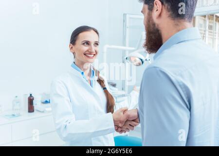 Porträt eines zuverlässigen und freundlichen weiblichen Zahnarzt oder Zahnarzt Schütteln der Hand eines Patienten in der Zahnarztpraxis einer modernen Klinik Stockfoto