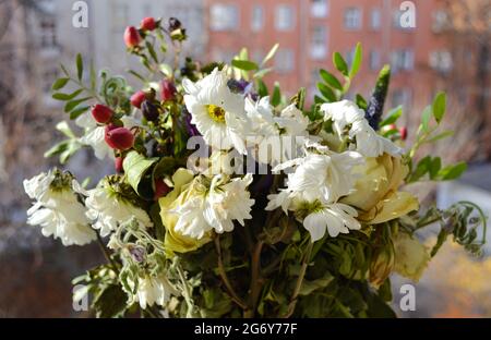 Ein verwelkter, gefrorener Strauß weißer Rosen und Chrysanthemen, Grün auf offenem Fenster vor dem Hintergrund der Straße und der Häuser. Das Ende des Urlaubs Stockfoto