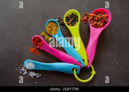 Nahaufnahme von bunten Messlöffeln in rosa, blauen und gelb-grünen Farben und verschiedenen Größen mit Gewürzen: Chili-Flocken, eine Mischung aus Pfeffererbsen, c Stockfoto