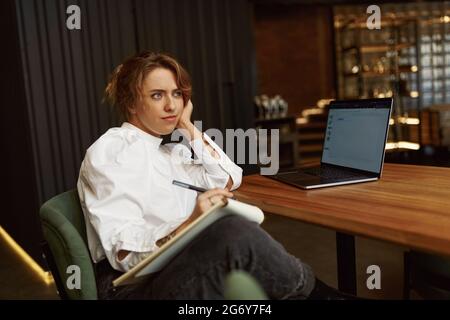 Nachdenkliche Frau, die mit einem Laptop im Café sitzt Stockfoto