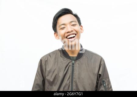 Junger Indonesier lacht fröhlich vor einem weißen Wandhintergrund Stockfoto