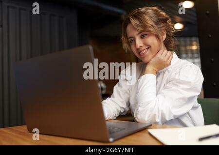 Lächelnde Frau in weißer Bluse, die am Laptop arbeitet Stockfoto