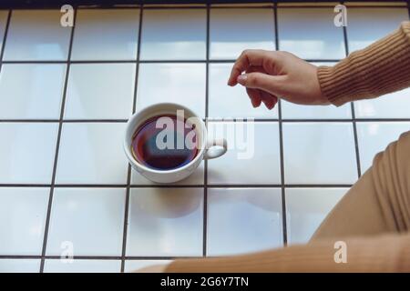 Nahaufnahme einer Frau, die mit einer Tasse Tee auf dem Fensterbrett sitzt Stockfoto