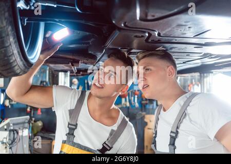 Zwei erfahrene Automechaniker analysieren zusammen die Felgen eines angehobenen Autos, während sie in einer modernen Kfz-Werkstatt arbeiten Stockfoto