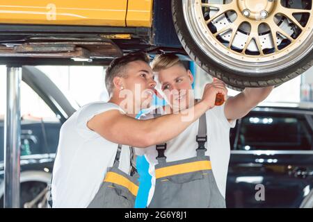 Zwei erfahrene Automechaniker analysieren zusammen die Felgen eines angehobenen Autos, während sie in einer modernen Kfz-Werkstatt arbeiten Stockfoto