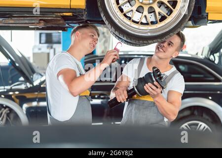 Zwei erfahrene Automechaniker analysieren zusammen die Felgen eines angehobenen Autos, während sie in einer modernen Kfz-Werkstatt arbeiten Stockfoto