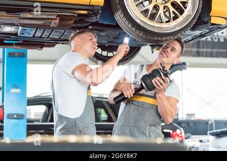 Zwei erfahrene Automechaniker analysieren zusammen die Felgen eines angehobenen Autos, während sie in einer modernen Kfz-Werkstatt arbeiten Stockfoto