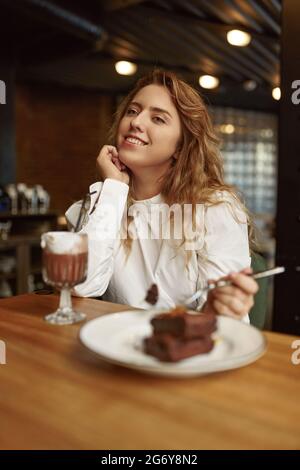 Entspannte Frau, die Kuchen isst und Kakao trinkt Stockfoto