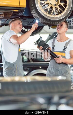 Zwei erfahrene Automechaniker analysieren zusammen die Felgen eines angehobenen Autos, während sie in einer modernen Kfz-Werkstatt arbeiten Stockfoto