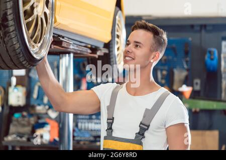 Porträt eines Auto-Tuning-Spezialisten lächelnd, während die Räder eines getunten gelüftelten Autos mit coolen modifizierten Felgen in einem trendigen Auto-Reparatur-Sho zu überprüfen Stockfoto