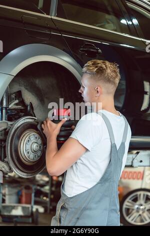 Erfahrener Automechaniker, der die Scheibenbremsen eines angehobenen Autos während der Arbeit in einer modernen Kfz-Werkstatt mit professionellen Tuning-Dienstleistungen ersetzt Stockfoto