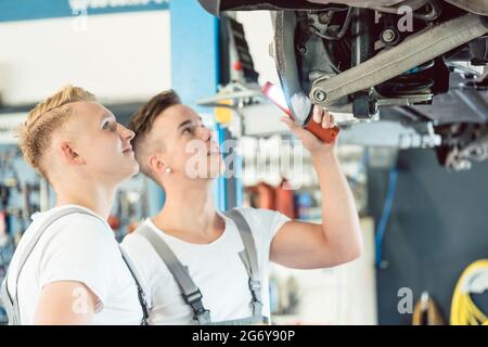 Porträt eines erfahrenen Automechanikers, der lächelt, während er einem Lehrling in einer modernen Kfz-Werkstatt über Scheibenbremsen unterrichtet Stockfoto