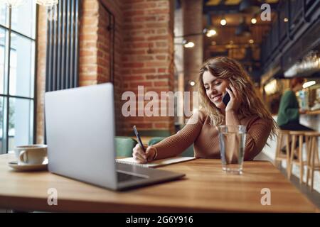Lächelnde Frau, die im Café sitzt und auf dem Handy spricht Stockfoto