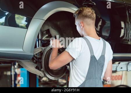 Erfahrener Automechaniker, der die Scheibenbremsen eines angehobenen Autos während der Arbeit in einer modernen Kfz-Werkstatt mit professionellen Tuning-Dienstleistungen ersetzt Stockfoto