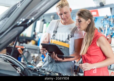 Zuverlässige Kfz-mechaniker mit einem weiblichen Kunden die Motor-fehlercodes durch ein Auto diagnostic Software in einem modernen Kfz-Werkstatt gescannt Stockfoto