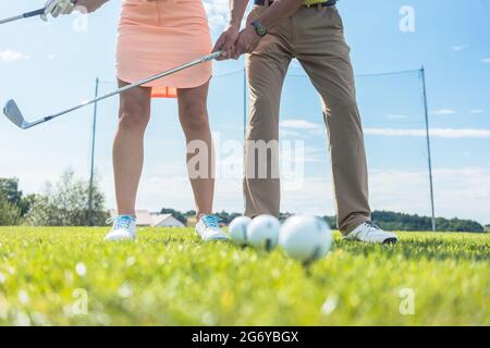 Niedriger Abschnitt von Mann und Frau, die Eisenkeule halten, während sie zusammen den richtigen Griff und die richtige Bewegung für das Golfspielen auf dem grünen Gras eines Spielers üben Stockfoto