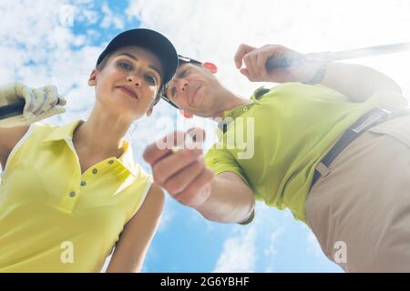 Porträt einer jungen Frau, die lächelt, während sie während eines professionellen Golfspiels mit ihrem Partner oder Lehrer im Freien die Kamera anschaut Stockfoto