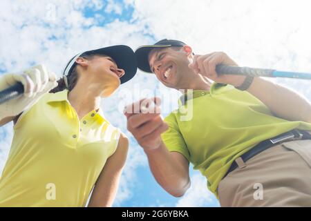 Porträt einer jungen Frau, die lächelt, während sie während eines professionellen Golfspiels mit ihrem Partner oder Lehrer im Freien die Kamera anschaut Stockfoto