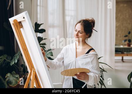 Frau, die mit Palette und Pinsel vor der Staffelei steht Stockfoto